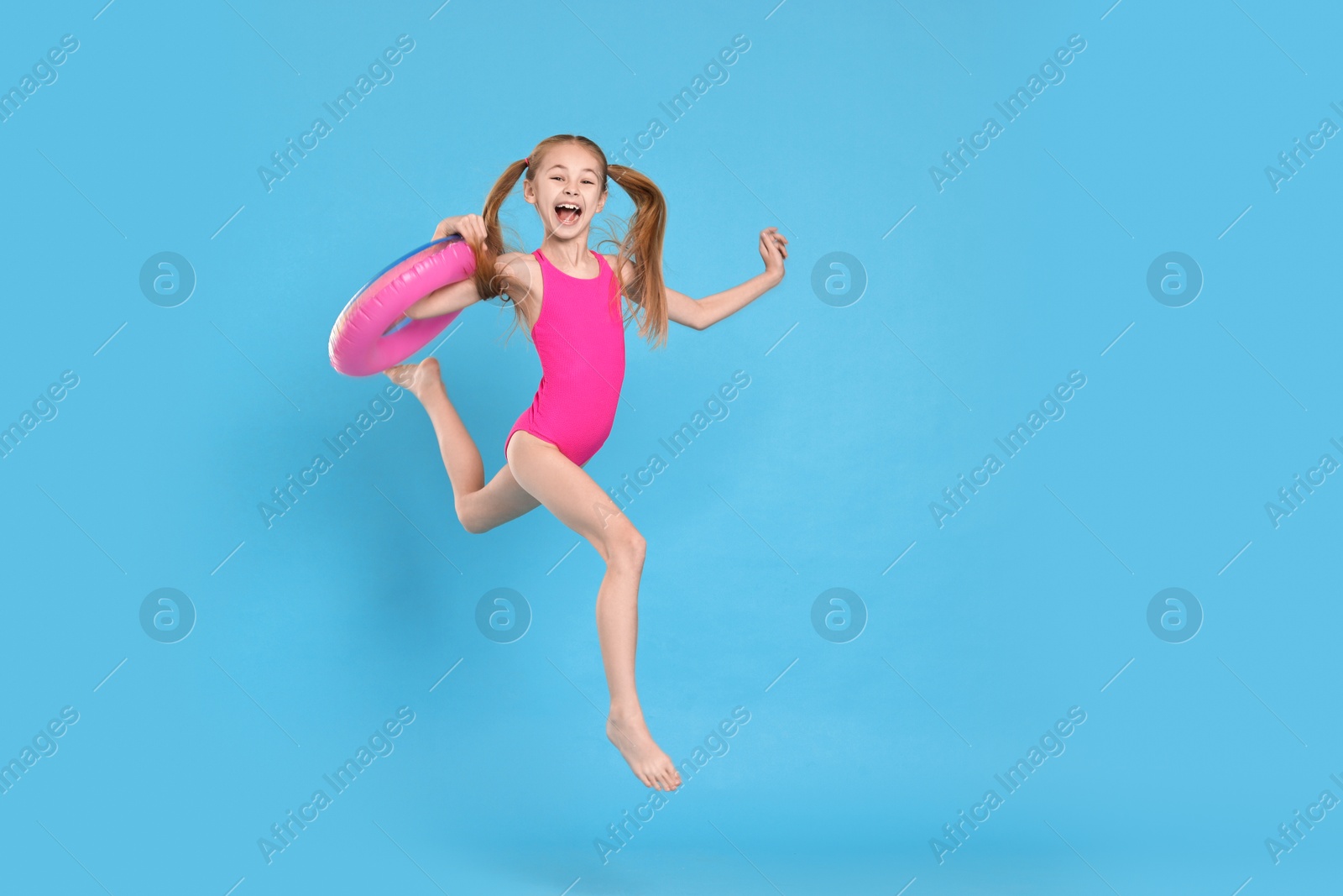 Photo of Happy girl in beachwear with inflatable ring jumping on light blue background