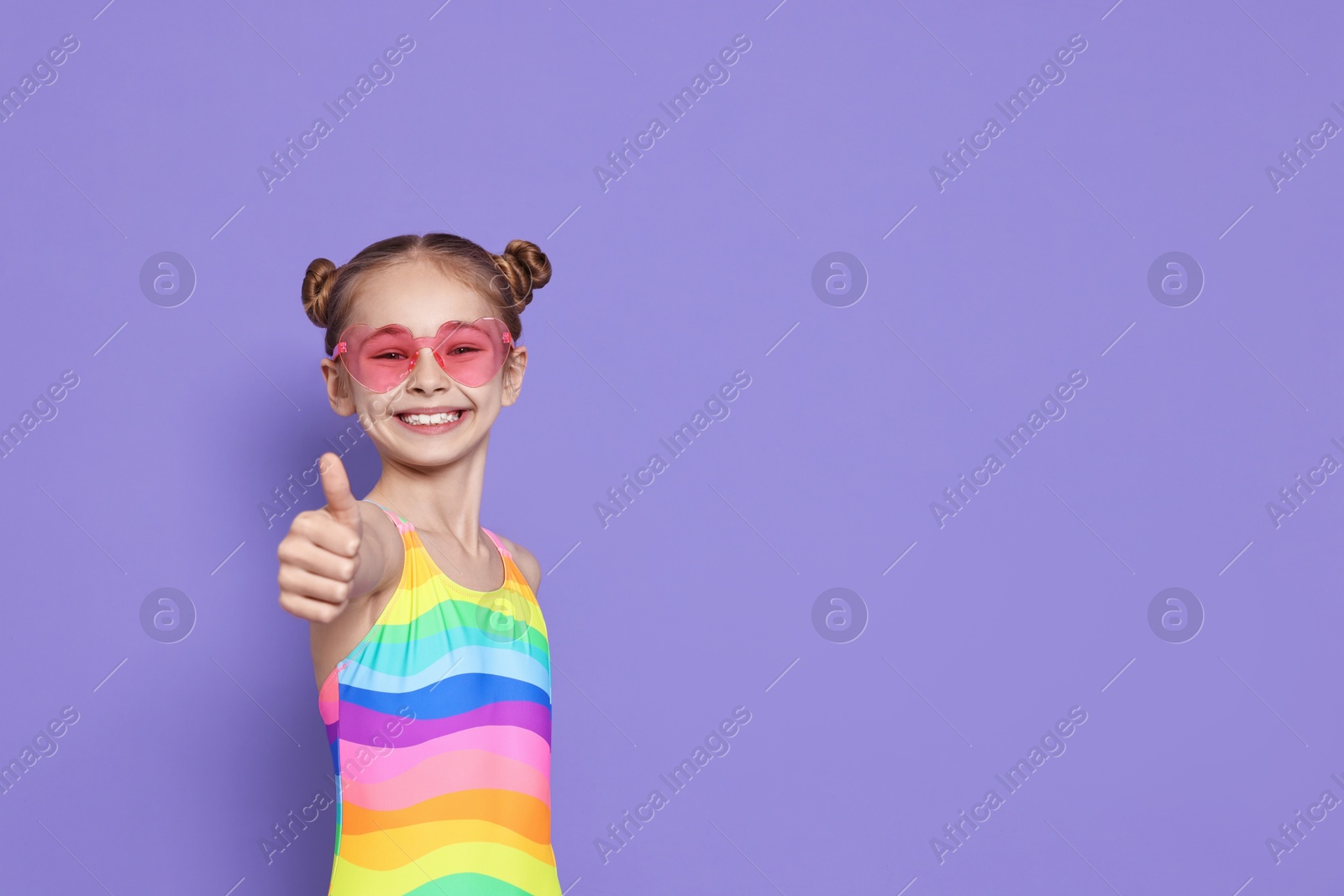 Photo of Happy girl in beachwear showing thumbs up on purple background, space for text