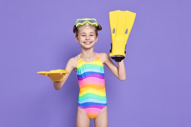 Photo of Happy girl in beachwear with diving mask and flippers on purple background