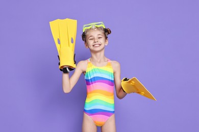 Photo of Happy girl in beachwear with diving mask and flippers on purple background