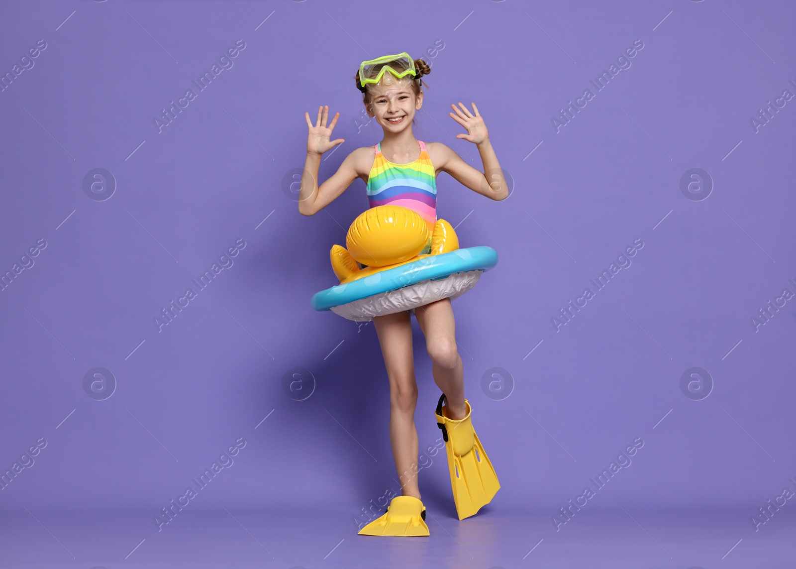 Photo of Happy girl in beachwear with diving mask, flippers and inflatable ring on purple background