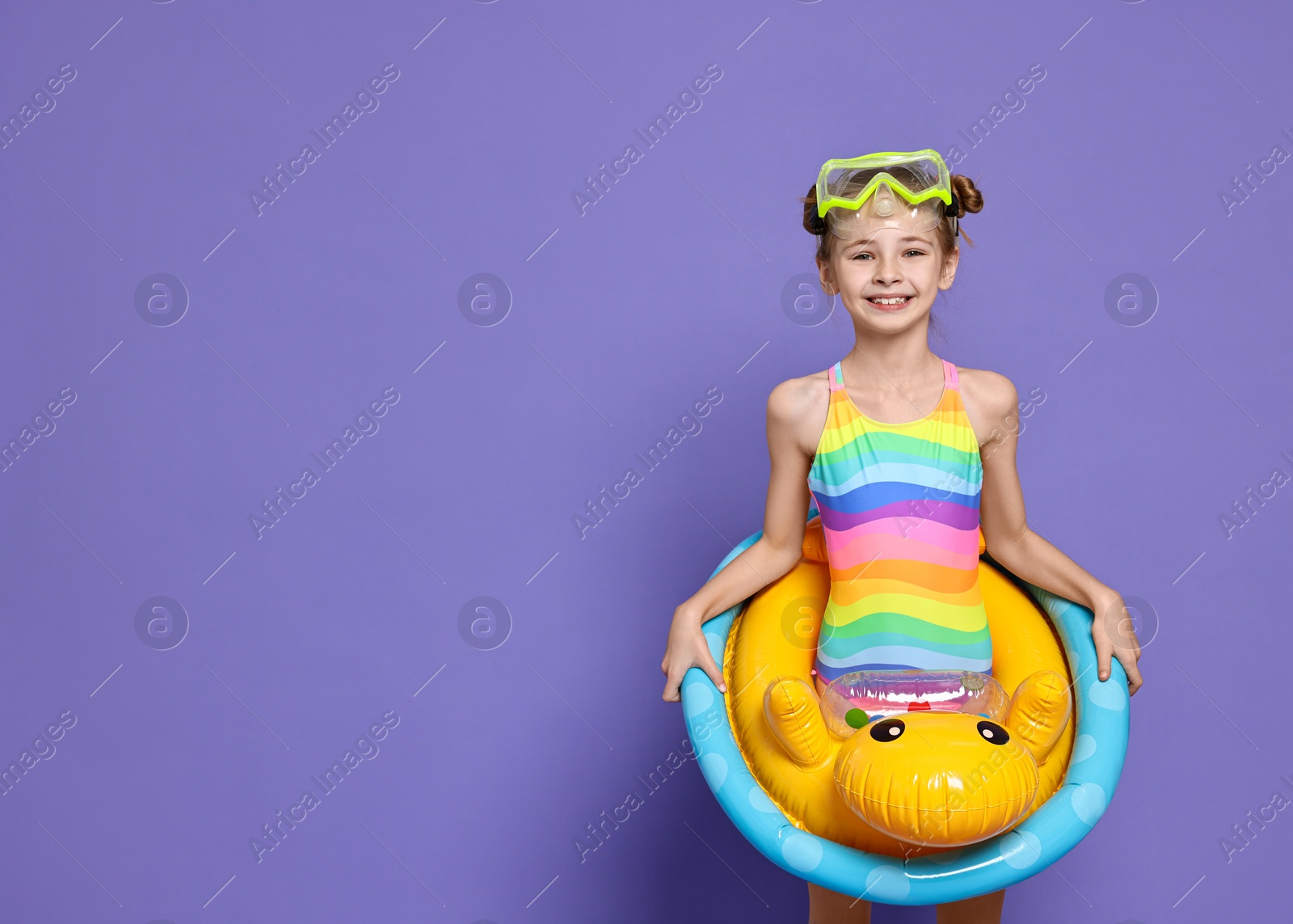 Photo of Happy girl in beachwear with diving mask and inflatable ring on purple background, space for text