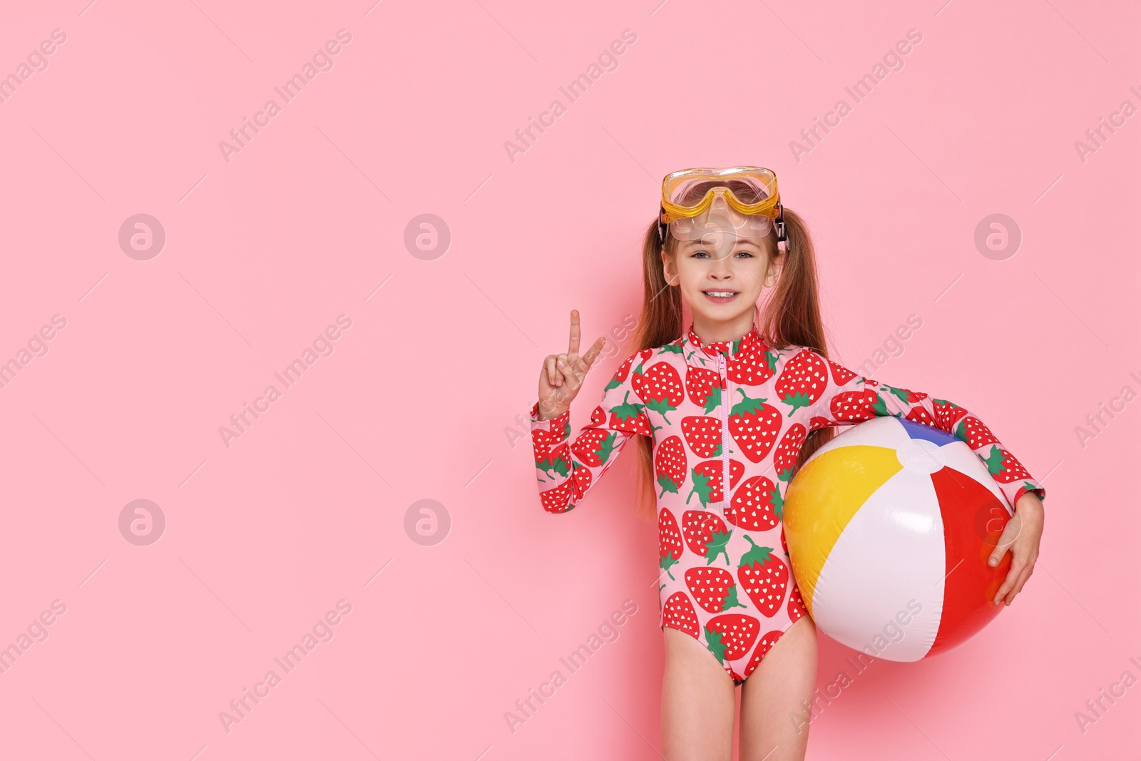 Photo of Happy girl in beachwear with diving mask and inflatable ball on pink background, space for text