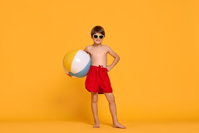 Photo of Little boy in beachwear with inflatable ball on orange background