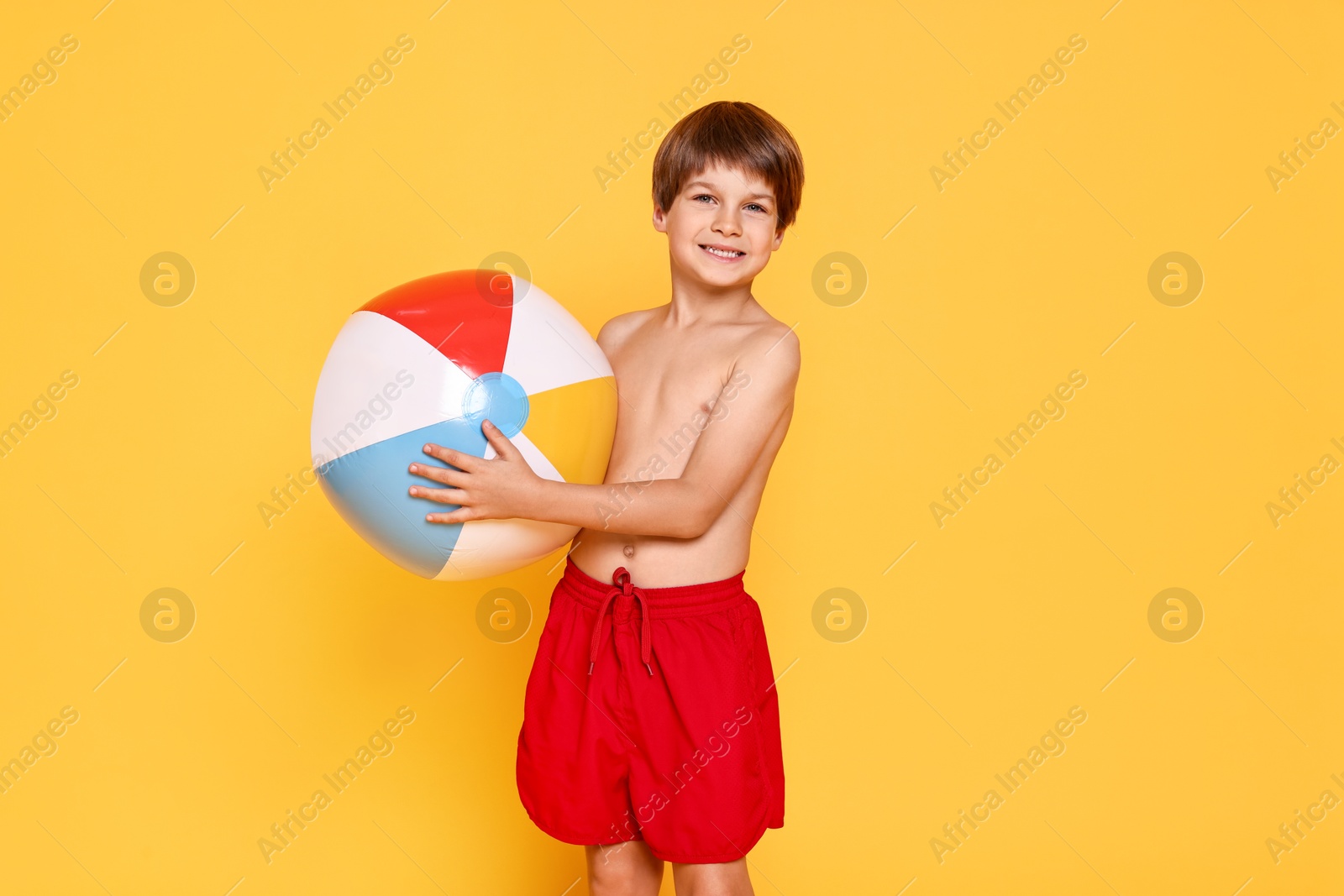 Photo of Little boy in beachwear with inflatable ball on orange background