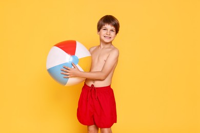 Photo of Little boy in beachwear with inflatable ball on orange background