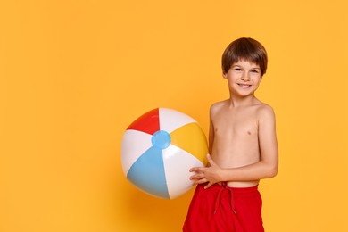 Photo of Little boy in beachwear with inflatable ball on orange background, space for text