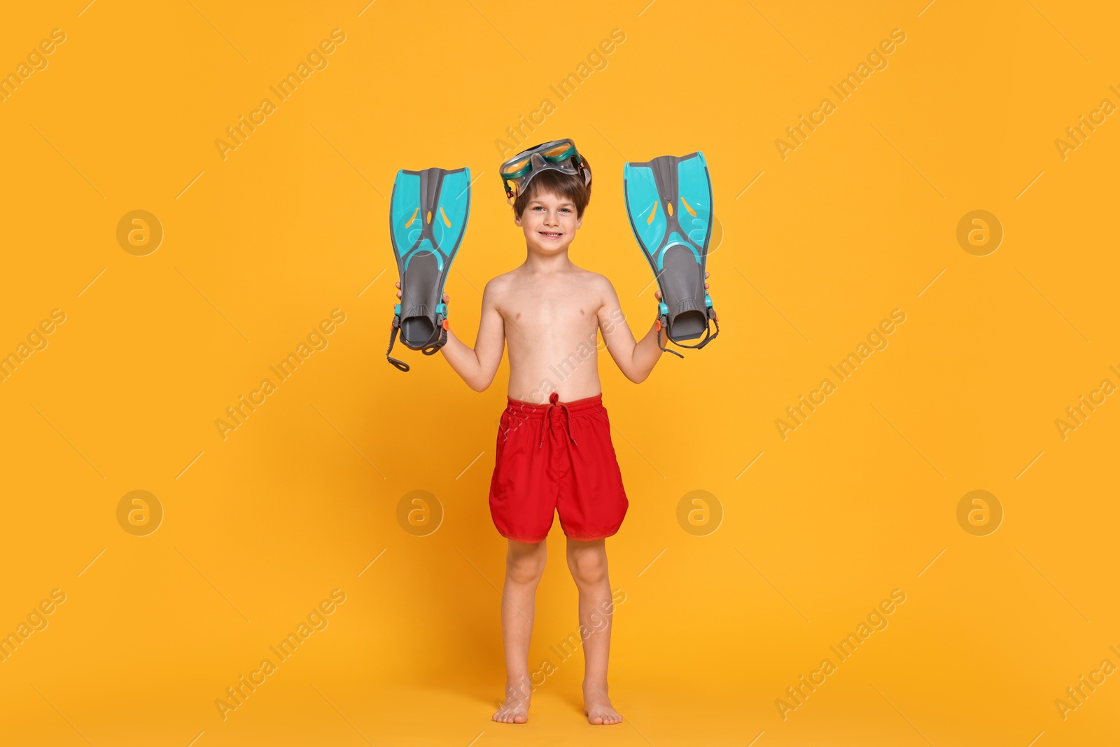 Photo of Little boy in beachwear with diving mask and flippers on orange background