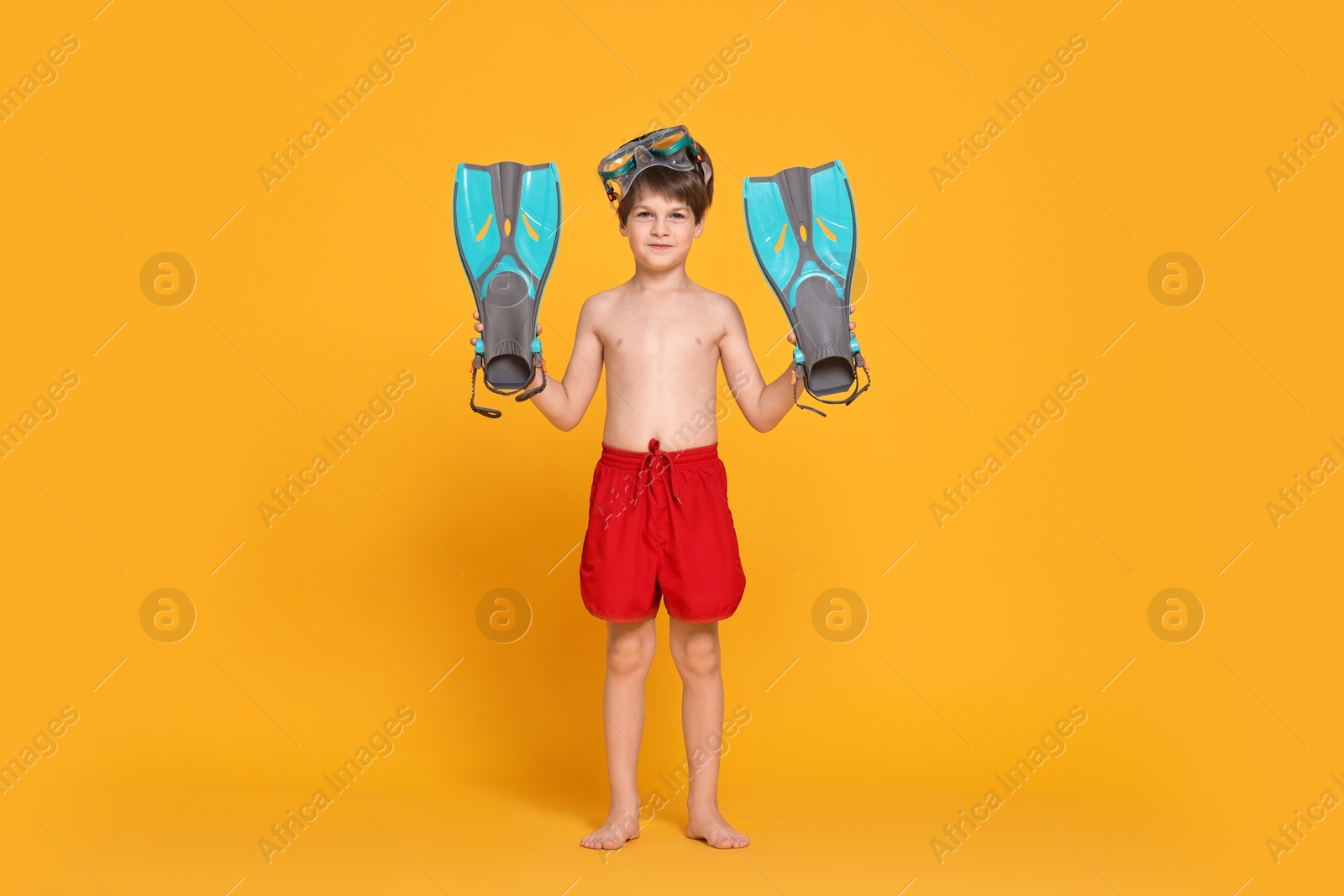 Photo of Little boy in beachwear with diving mask and flippers on orange background