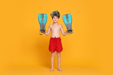 Photo of Little boy in beachwear with diving mask and flippers on orange background