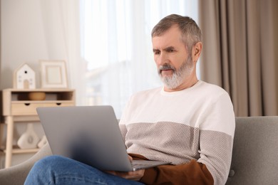 Mature man with laptop on sofa at home