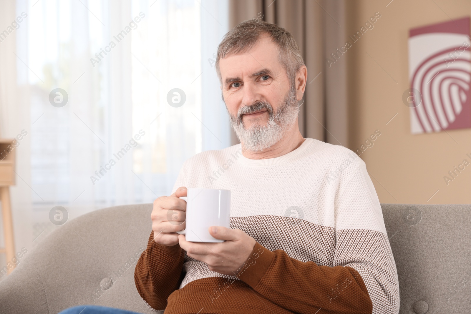 Photo of Mature man with cup of hot drink on sofa at home. Space for text