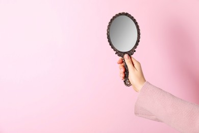 Woman holding vintage mirror on pink background, closeup. Space for text