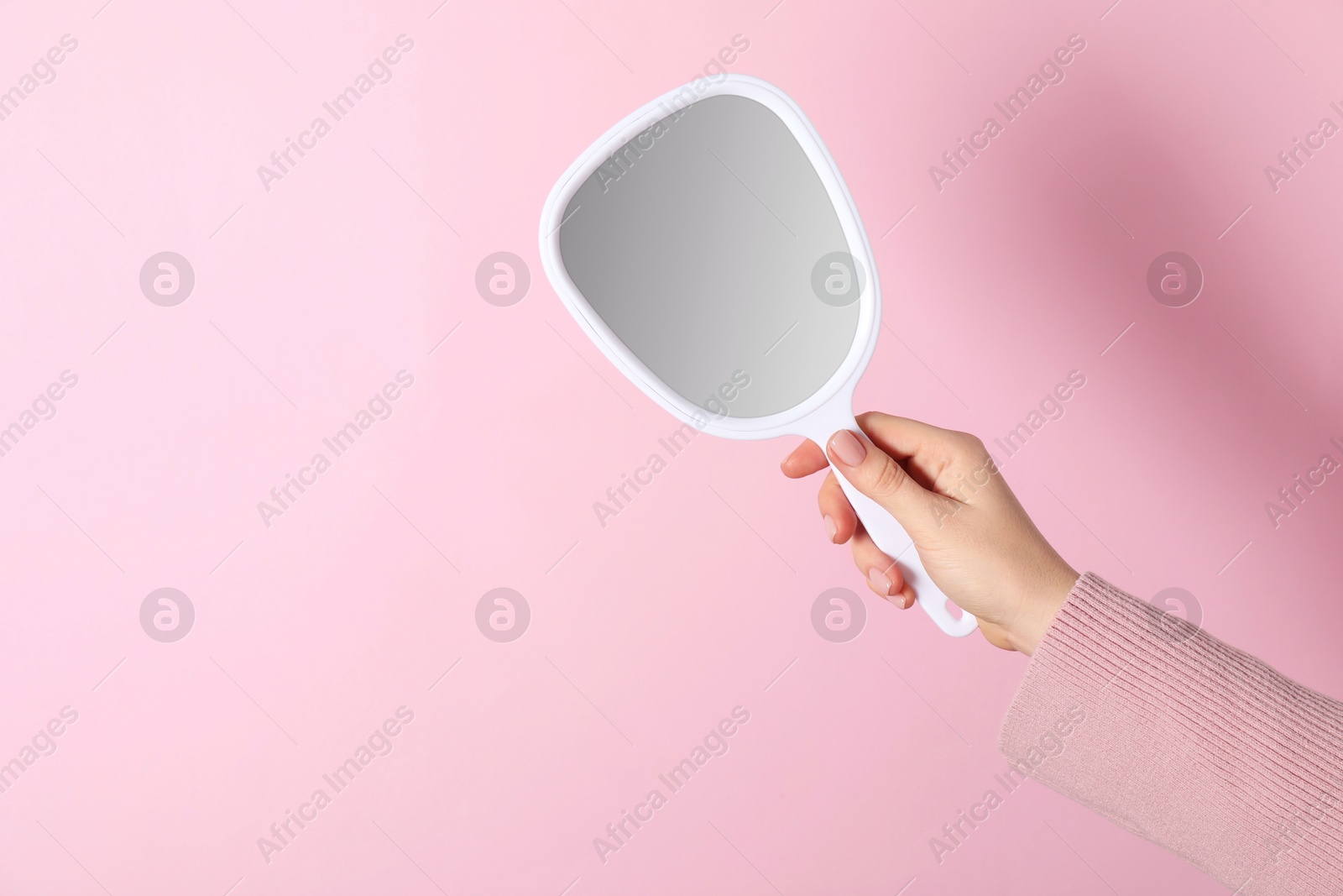 Photo of Woman holding small mirror on pink background, closeup. Space for text