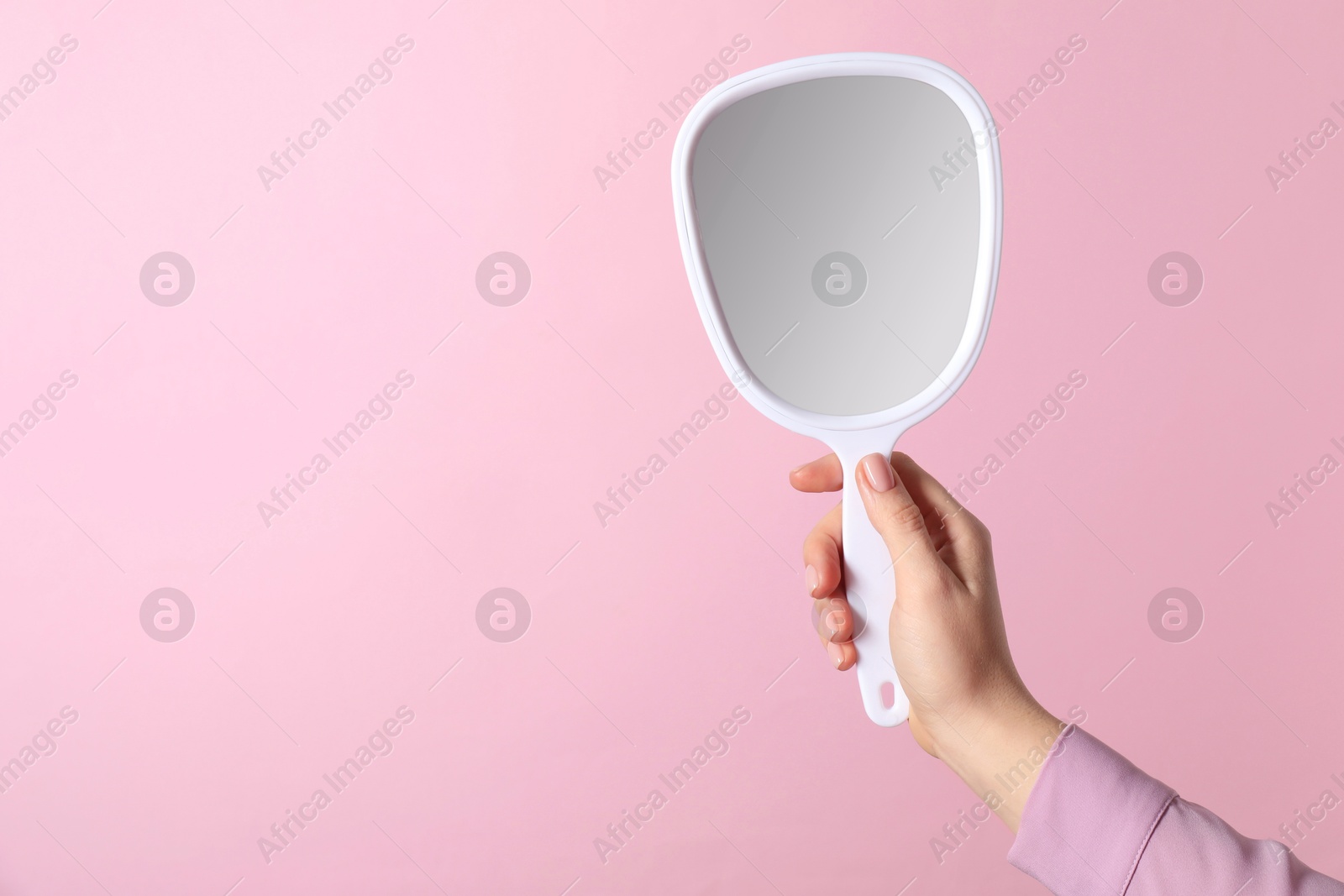 Photo of Woman holding small mirror on pink background, closeup. Space for text