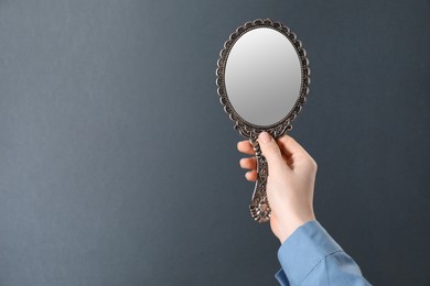 Woman holding vintage mirror on grey background, closeup. Space for text