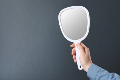 Woman holding small mirror on grey background, closeup. Space for text