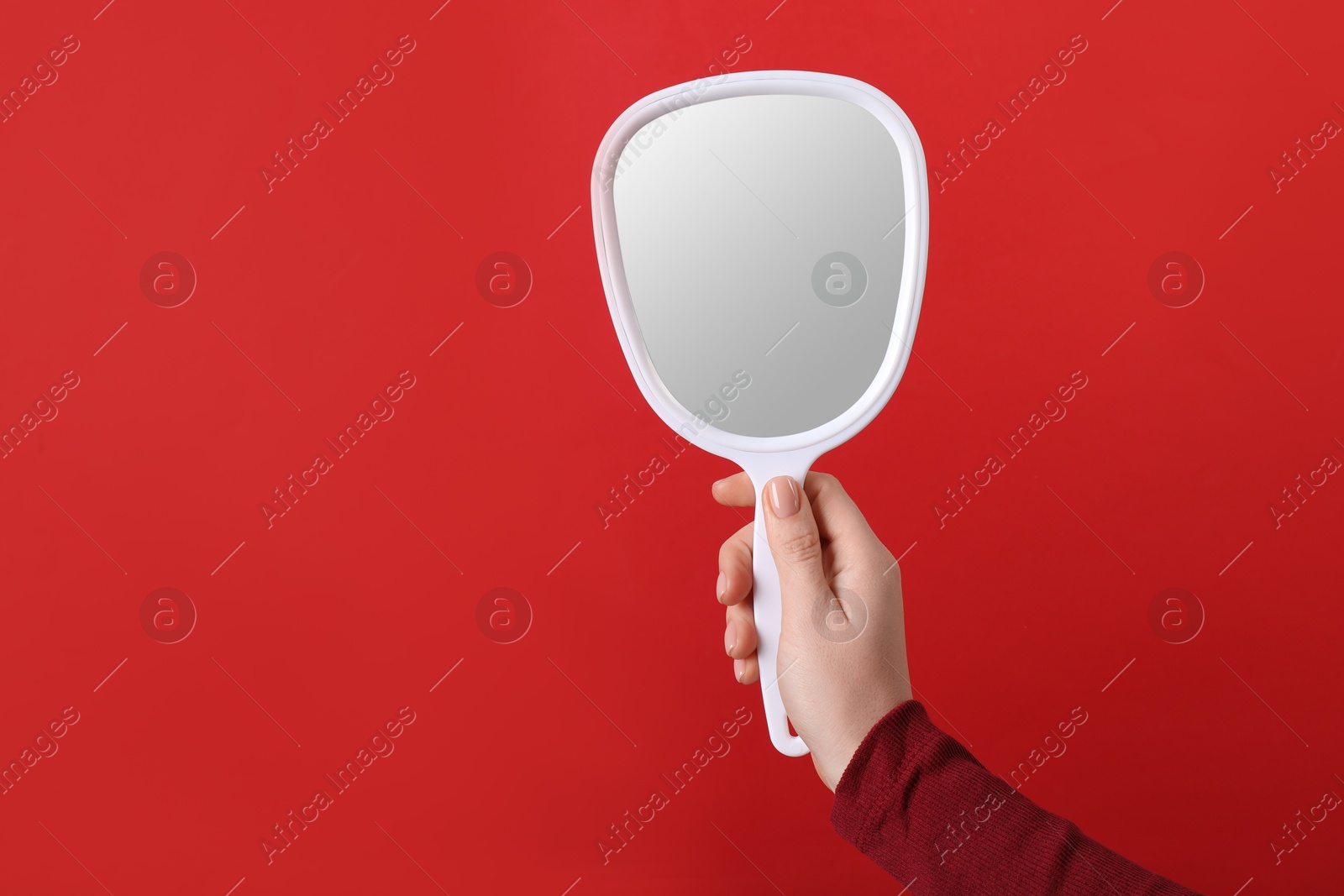 Photo of Woman holding small mirror on red background, closeup. Space for text