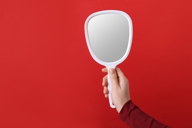 Photo of Woman holding small mirror on red background, closeup. Space for text