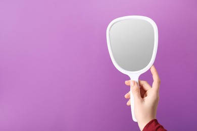 Photo of Woman holding small mirror on purple background, closeup. Space for text