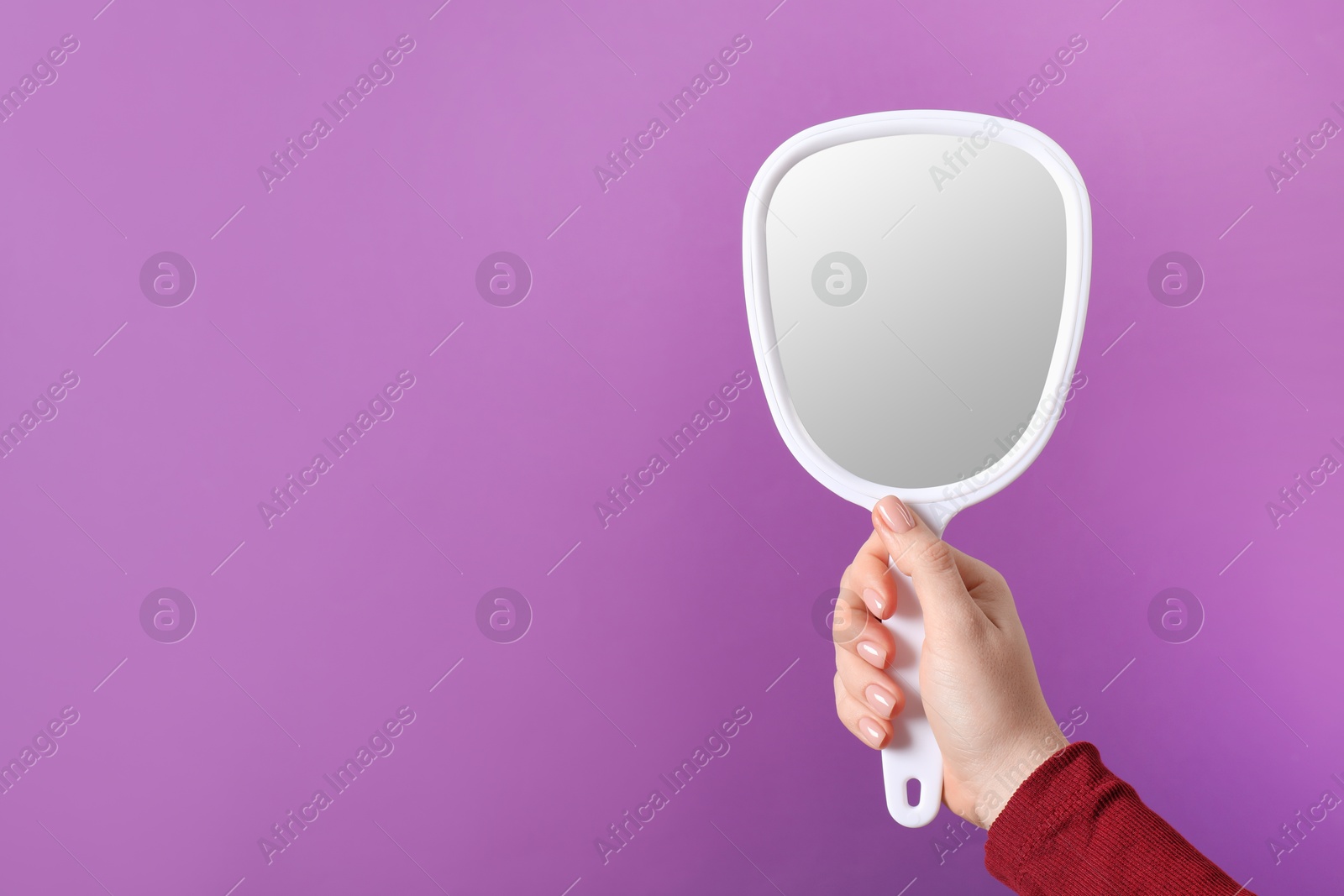 Photo of Woman holding small mirror on purple background, closeup. Space for text