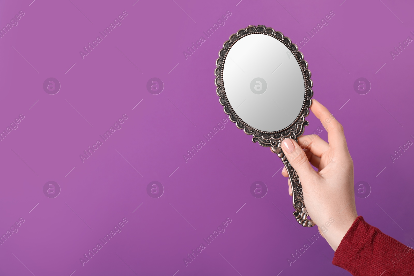 Photo of Woman holding vintage mirror on purple background, closeup. Space for text