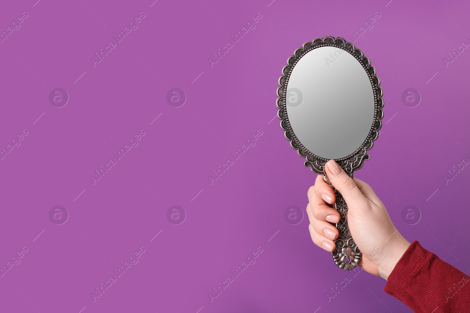 Photo of Woman holding vintage mirror on purple background, closeup. Space for text