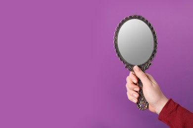 Photo of Woman holding vintage mirror on purple background, closeup. Space for text