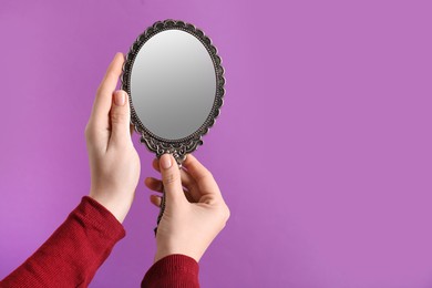 Photo of Woman holding vintage mirror on purple background, closeup. Space for text