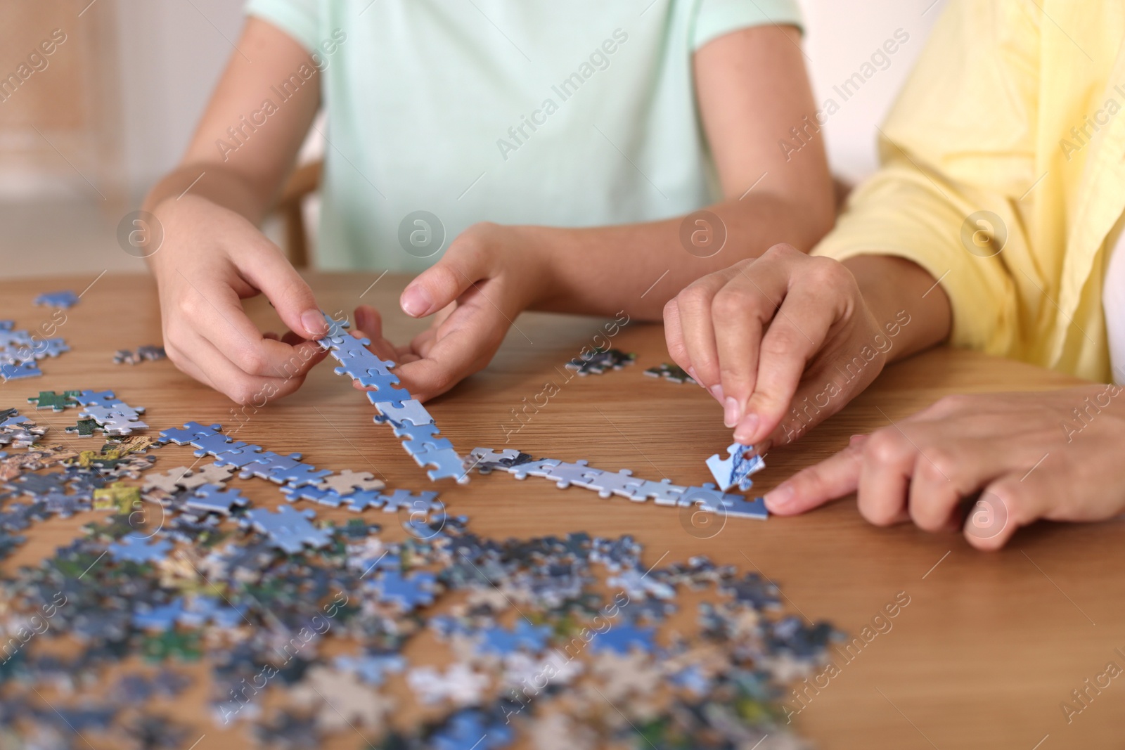 Photo of Mother and her daughter solving puzzle together at wooden table indoors, closeup