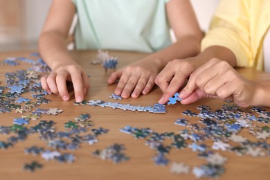 Mother and her daughter solving puzzle together at wooden table indoors, closeup