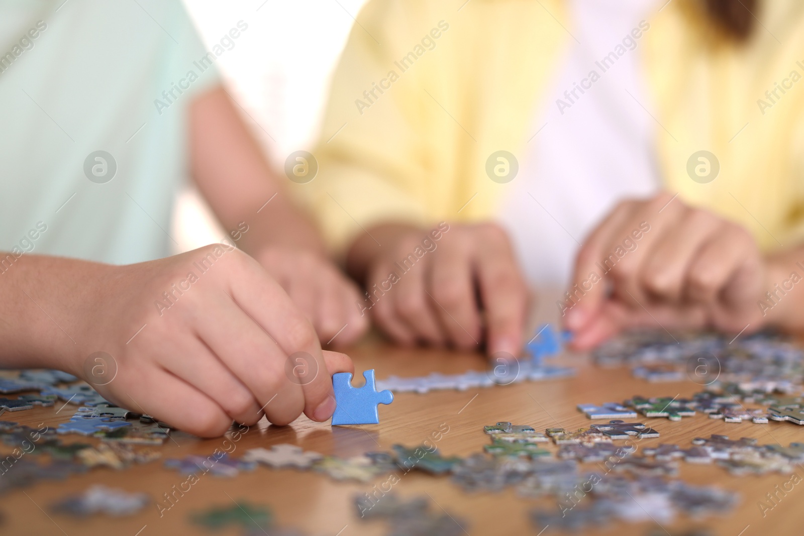 Photo of Mother and her daughter solving puzzle together at wooden table indoors, closeup