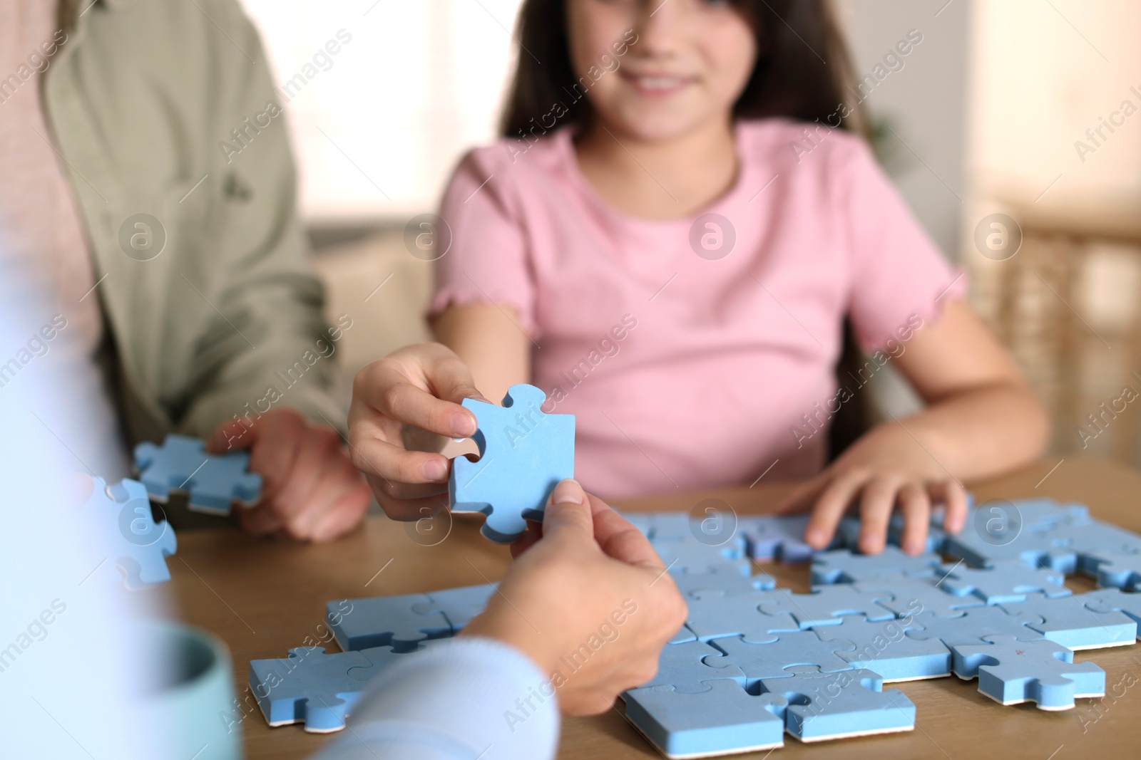 Photo of Parents and their daughter solving puzzle together at wooden table indoors, closeup