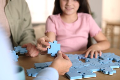 Parents and their daughter solving puzzle together at wooden table indoors, closeup