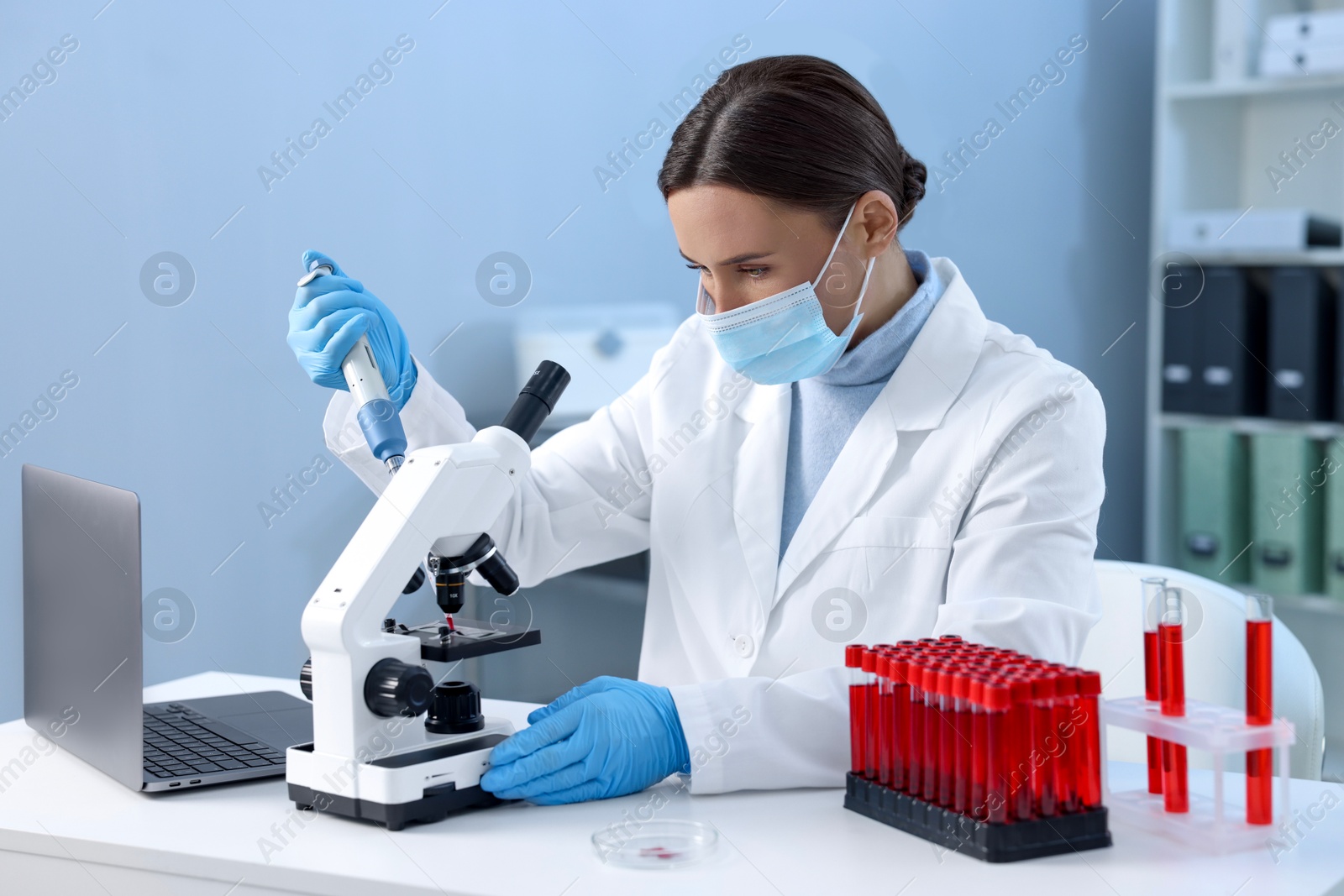 Photo of Laboratory testing. Doctor dripping blood sample onto glass slide while working with microscope at table indoors