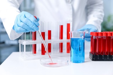 Photo of Laboratory testing. Doctor dripping blood sample into Petri dish at table indoors, closeup