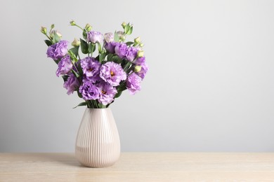 Photo of Vase with beautiful eustoma flowers on wooden table, space for text