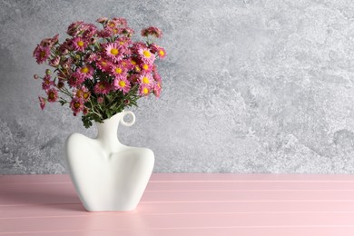 Photo of Stylish vase with beautiful flowers on pink wooden table. Space for text