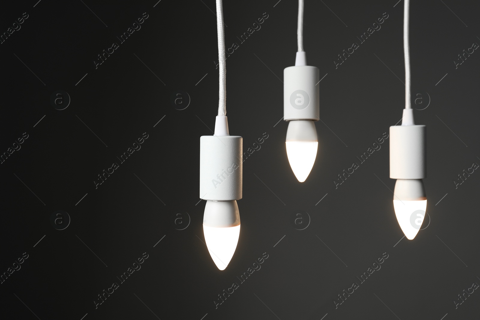 Photo of Light bulbs hanging on cords against grey background, space for text