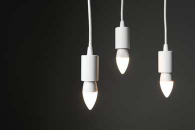 Photo of Light bulbs hanging on cords against grey background, space for text