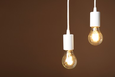 Photo of Light bulbs hanging on cords against brown background, space for text