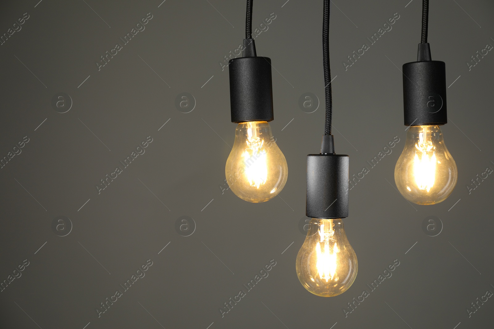 Photo of Light bulbs hanging on cords against grey background, space for text