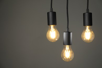 Photo of Light bulbs hanging on cords against grey background, space for text