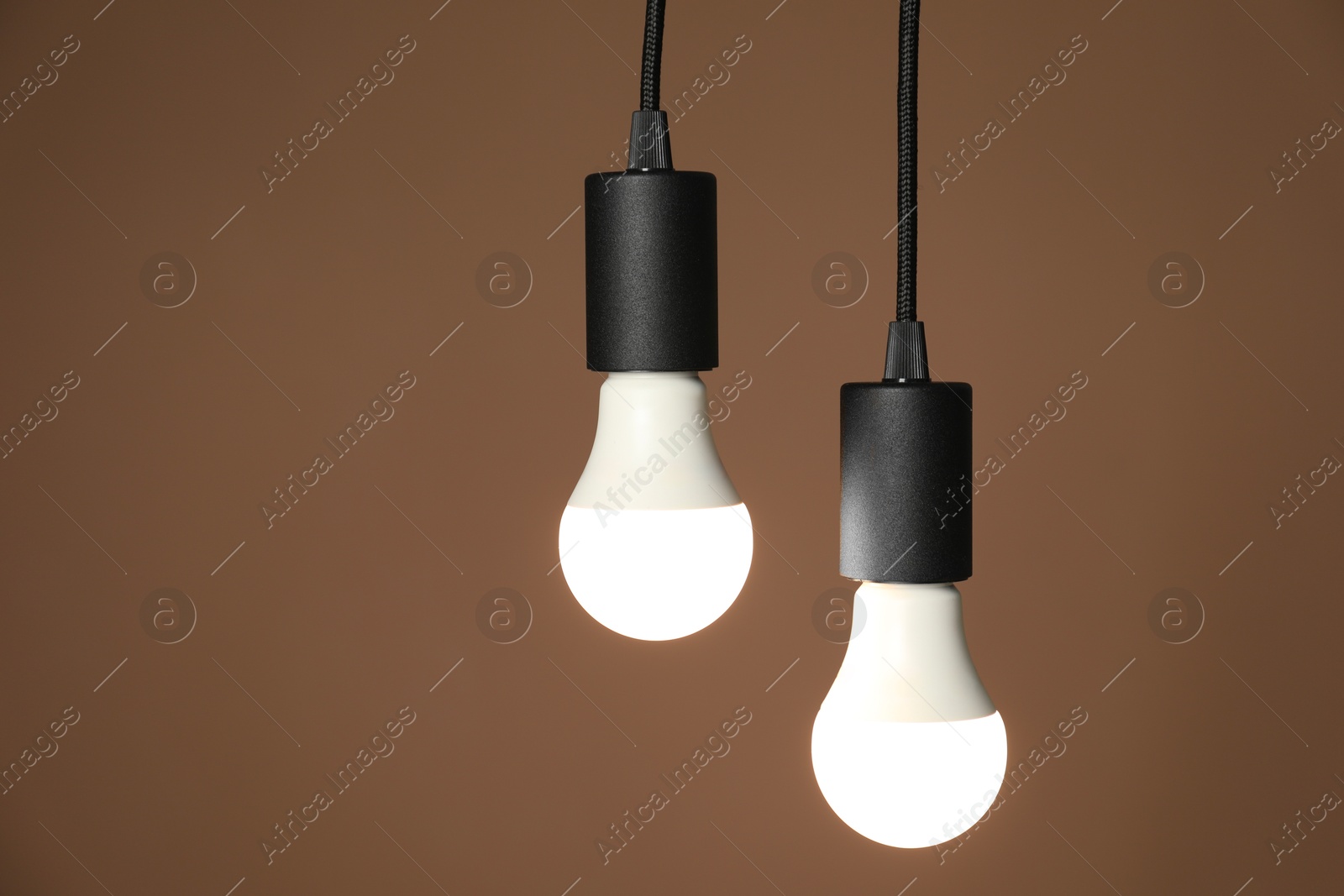 Photo of Light bulbs hanging on cords against brown background, space for text