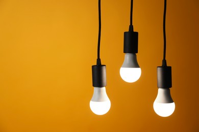 Photo of Light bulbs hanging on cords against orange background, space for text