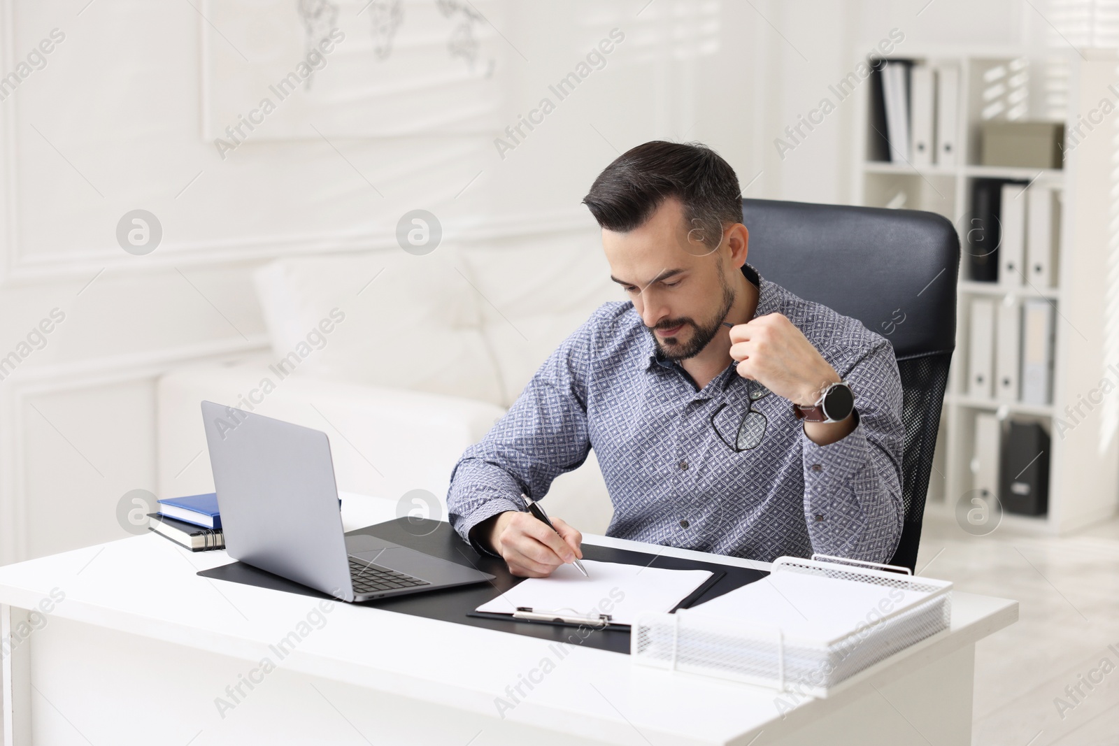 Photo of Handsome banker signing document at table in office