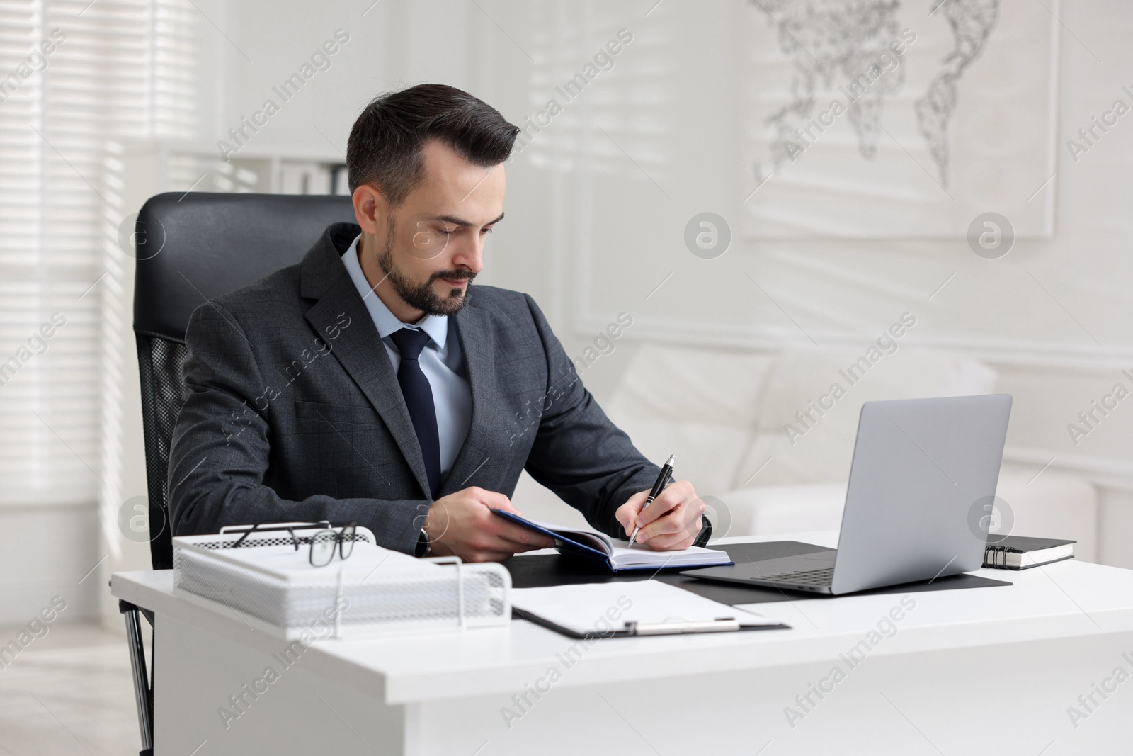 Photo of Handsome banker making notes at table in office