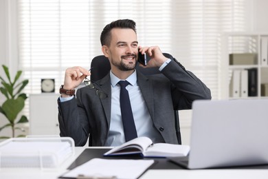 Photo of Happy banker talking on smartphone at table in office