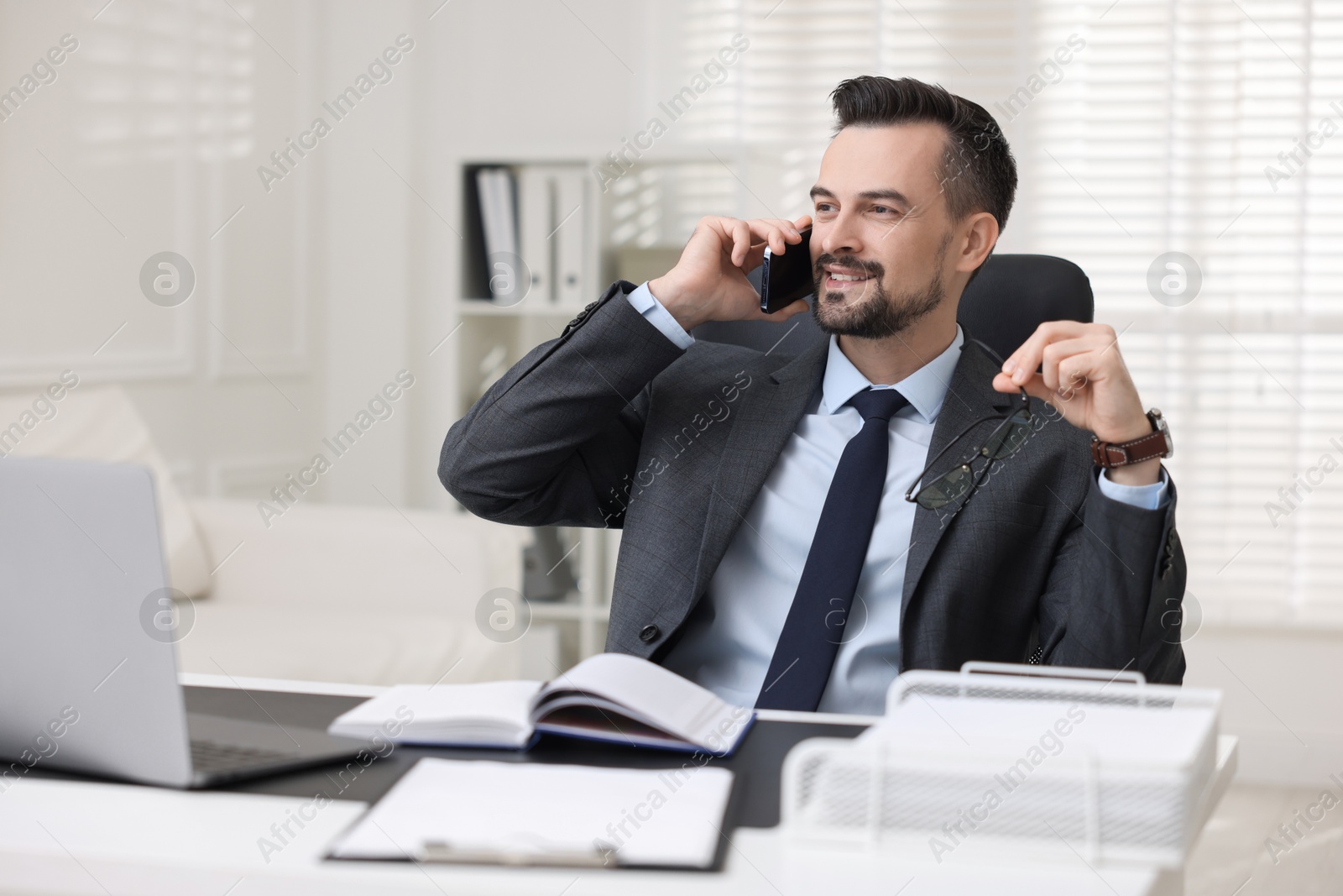 Photo of Happy banker talking on smartphone at table in office