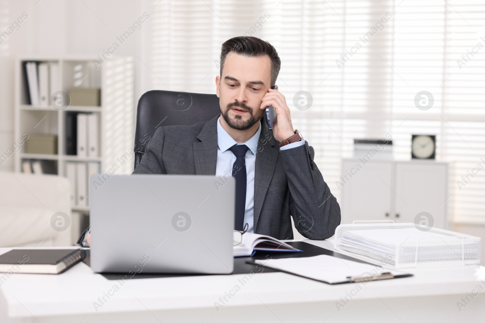 Photo of Handsome banker talking on smartphone at table in office